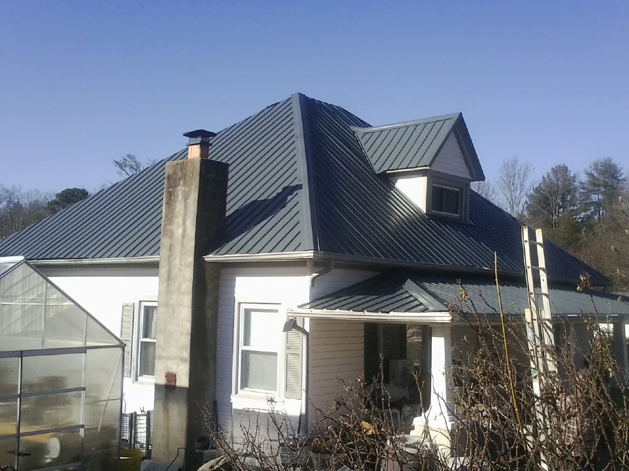 Dark blue standing seam metal roof on a white farmhouse with dormer — Slate & Tile Roof Repair by Roofing Brothers in Maybrook