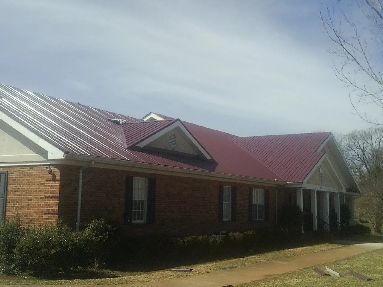 Red metal roof with gabled entries on a long brick building, from a Hail Damage Roof Repair job in Maybrook