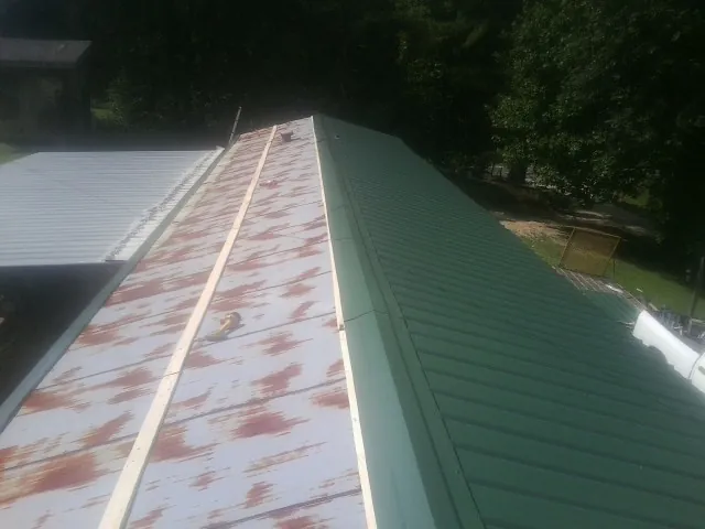 Old rusted panels beside newly installed green metal roofing — Wind Damage Roof Repair by Roofing Brothers in Maybrook