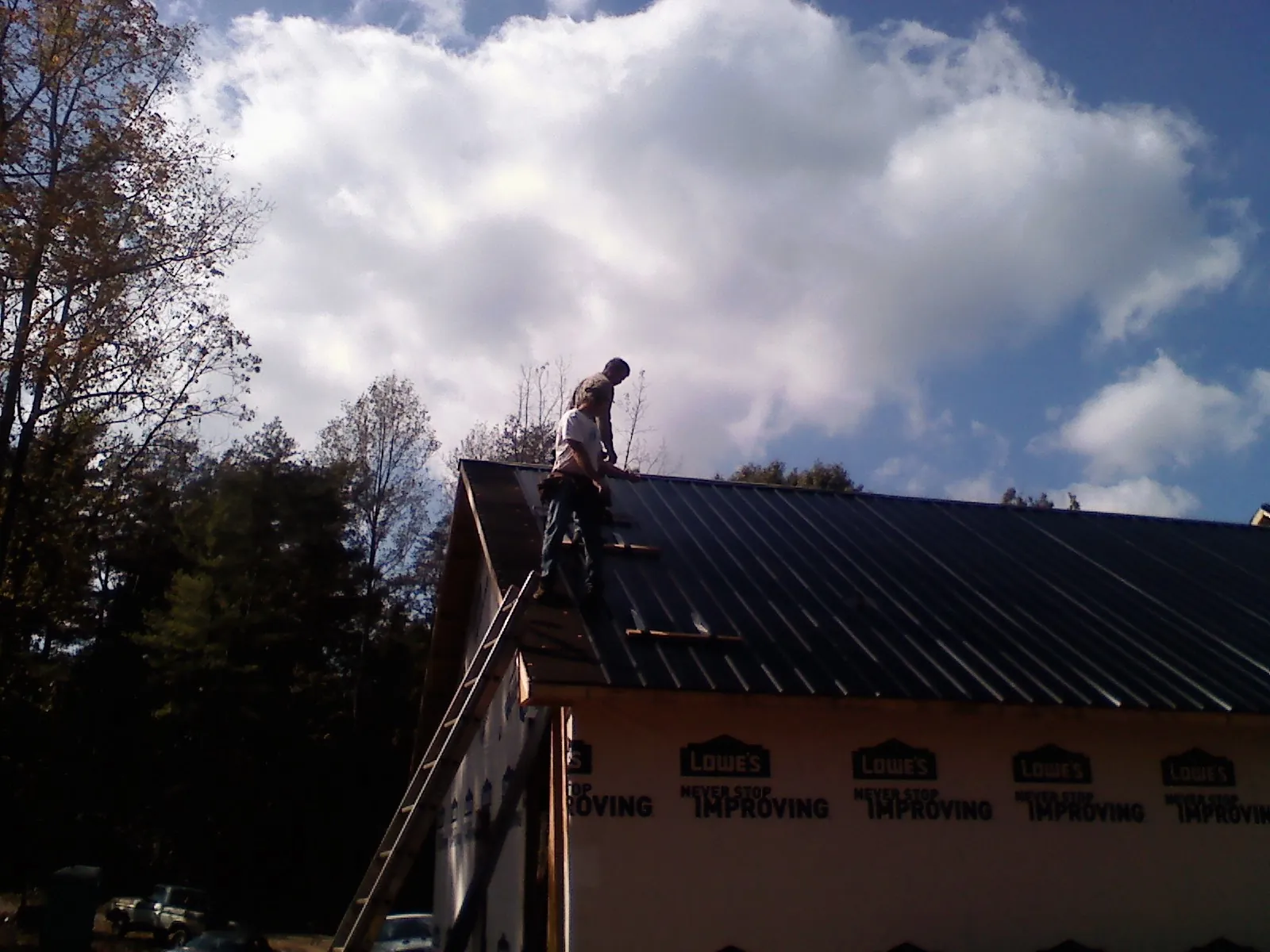 Roofer fastening dark metal panels high against a cloudy sky, from a Roof Inspection job in Maybrook