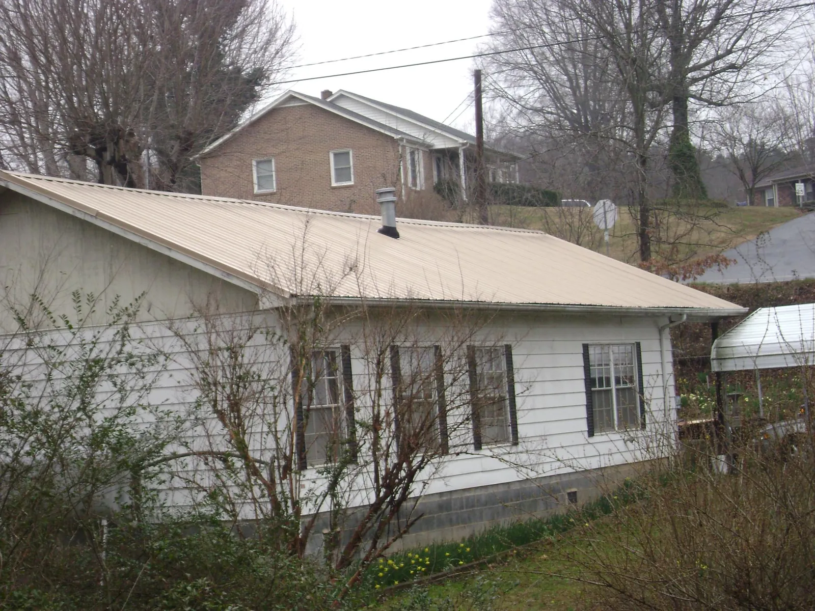 Tan metal roof on a white sided house set into a hillside — Commercial Roofing by Roofing Brothers in Maybrook